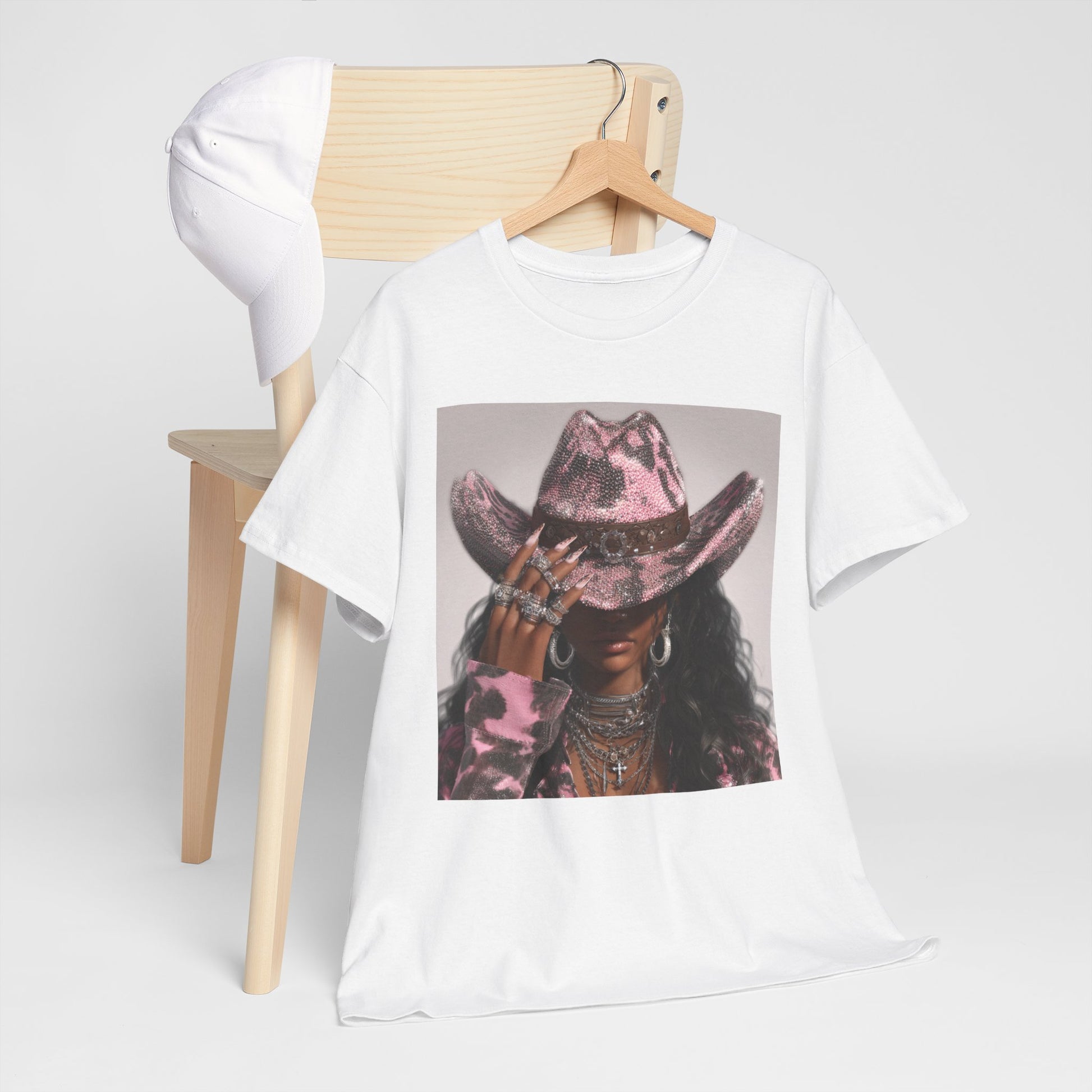 White t-shirt with a graphic of a person wearing a pink cowboy hat on a wooden chair.